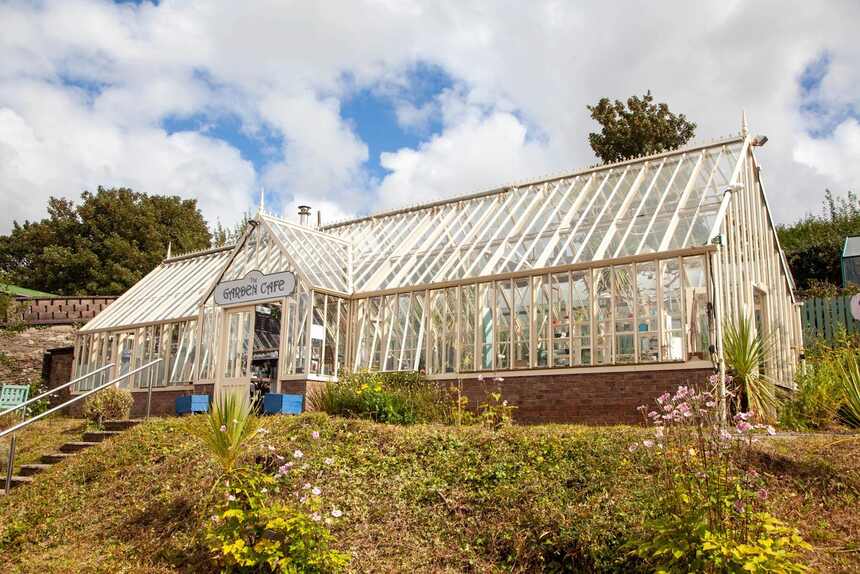The cream Victorian-style glasshouse with the Garden Cafe sign over the door, steps and planting in front.